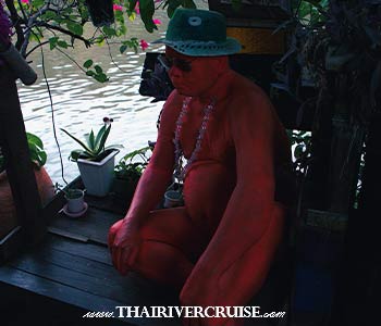 The Iconic Red Man Statue: Keep an eye out for the eye-catching, life-sized red human sculpture sitting prominently on the wooden terrace by the water, endlessly gazing at the passing long-tail boats. - Khlong Bang Luang Floating Market The Iconic Red Man Statue: Keep an eye out for the eye-catching, life-sized red human sculpture sitting prominently on the wooden terrace by the water, endlessly gazing at the passing long-tail boats. - Khlong Bang Luang Floating Market