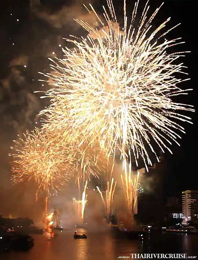 Large, sparkling golden firework bursts and ground-based fountains launch over the Chao Phraya River, with the Bangkok city skyline under a dark sky.