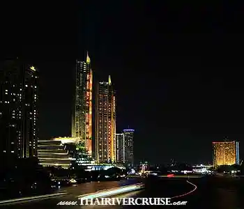 Horizontal night view capturing the modern, lit-up high-rise buildings and skyscrapers along the curve of the Chao Phraya River. Light trails from river traffic are visible on the water, and key buildings like ICONSIAM are visible among the cityscape Horizontal night view capturing the modern, lit-up high-rise buildings and skyscrapers along the curve of the Chao Phraya River. Light trails from river traffic are visible on the water, and key buildings like ICONSIAM are visible among the cityscape