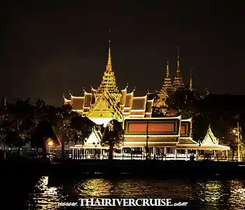 Horizontal landscape view across the dark Chao Phraya River of the gilded spires, rooftops, and pavilions of the Grand Palace complex, including Wat Phra Kaew, illuminated in a warm, majestic glow. The dark riverbank and reflections frame the historic site under a night sky. Horizontal landscape view across the dark Chao Phraya River of the gilded spires, rooftops, and pavilions of the Grand Palace complex, including Wat Phra Kaew, illuminated in a warm, majestic glow. The dark riverbank and reflections frame the historic site under a night sky.